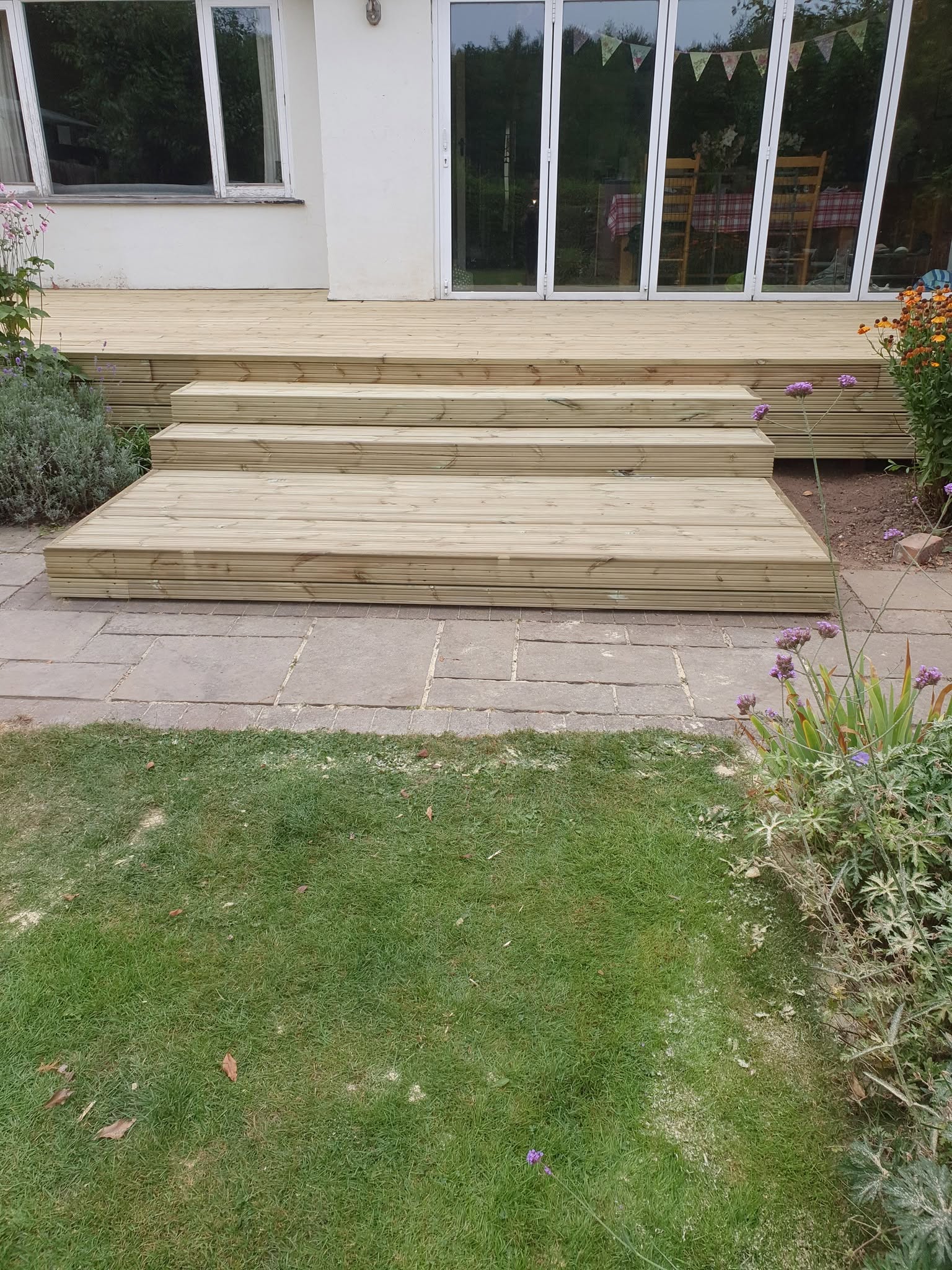 Softwood garden decking with wide tiered steps leading to bifold doors by LMB Joinery.